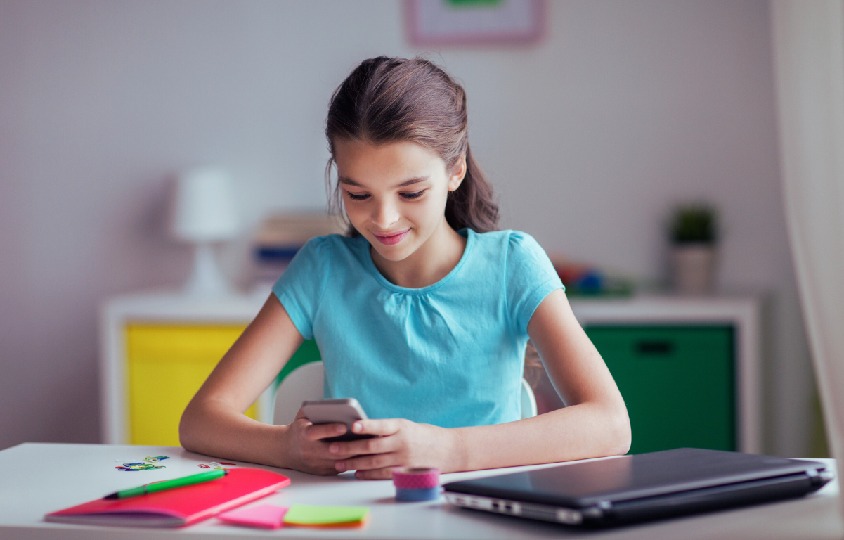 Ein Mädchen schaut lächelnd auf sein Handy, während es Hausaufgaben macht