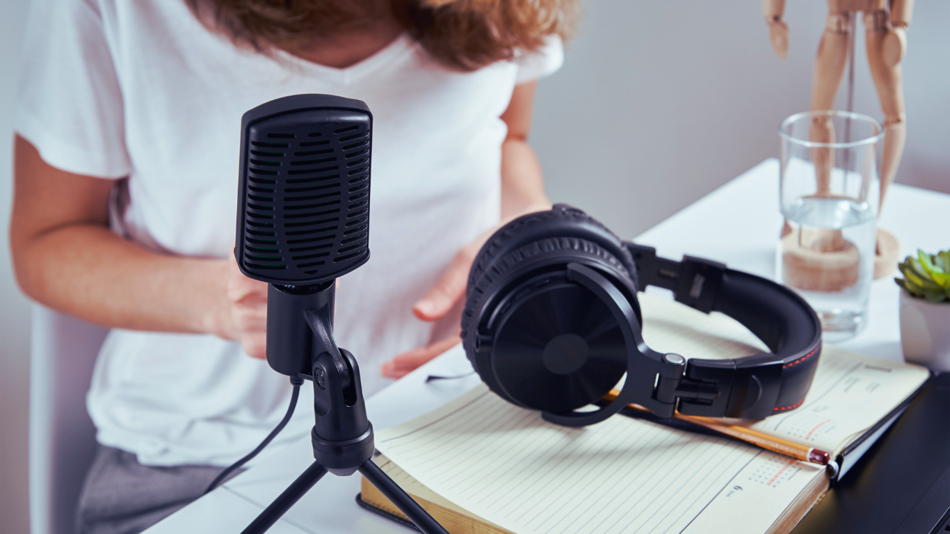 Eine Person, die einen Podcast aufnimmt. Neben ihr liegen Kopfhörer und ein Mikrophon.