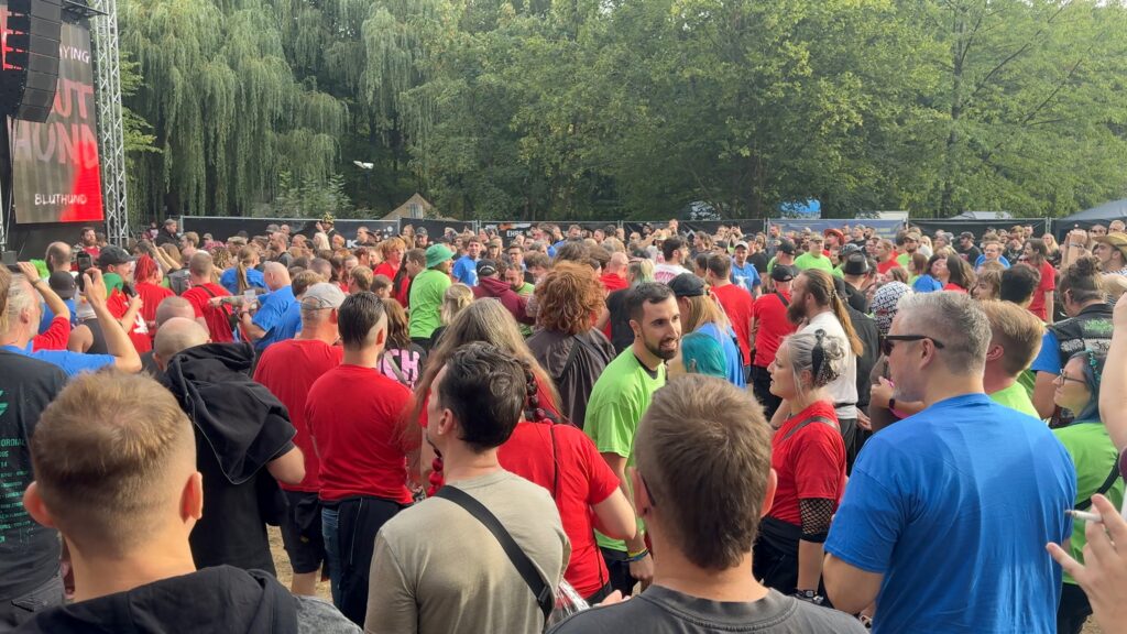 Eine große Menge von Personen in roten, grünen und blauen T-Shirts vor einer Bühne.
